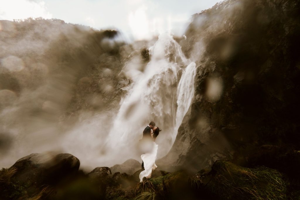 Bride and Groom in Wedding Attire Embracing in Front Of Waterfall