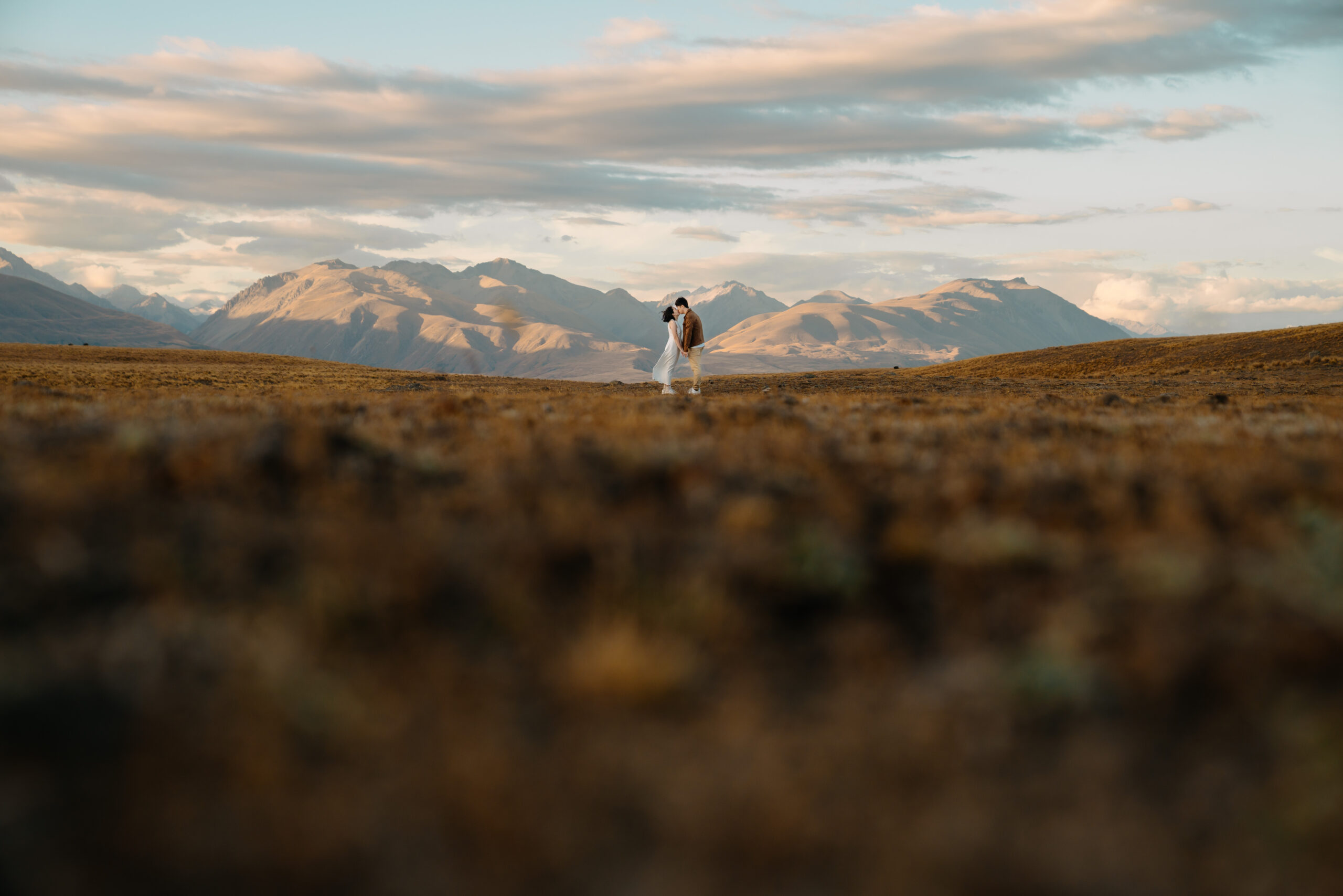 Couple kissing after their proposal standing with a beautiful backdrop of mountains surrounding Tekapo
