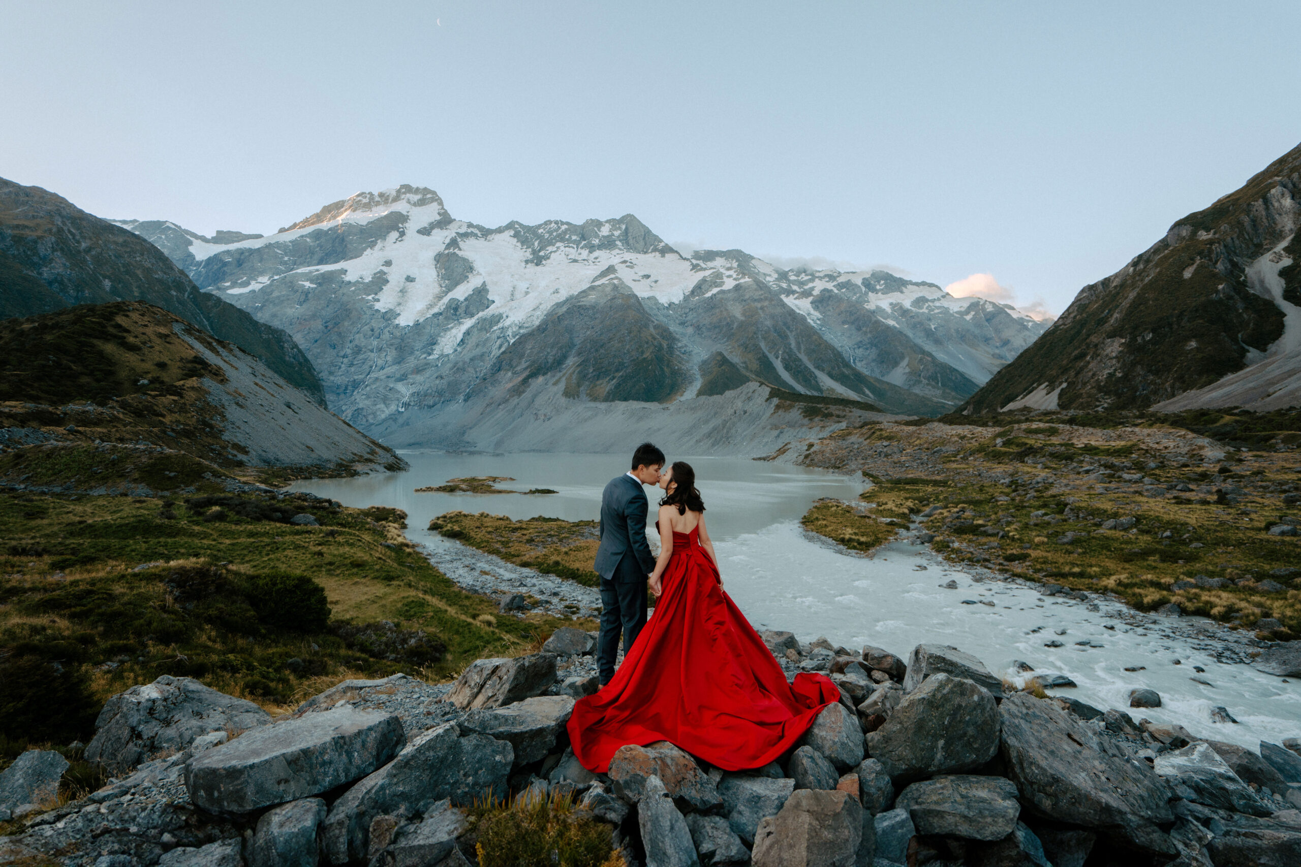 A couple kissing in Mount Cook National Park wearing a red dress and blue suit