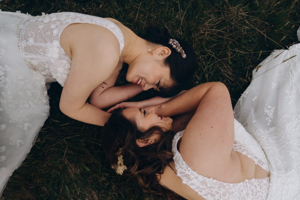 Two brides lying in a field in New Zealand facing eachother